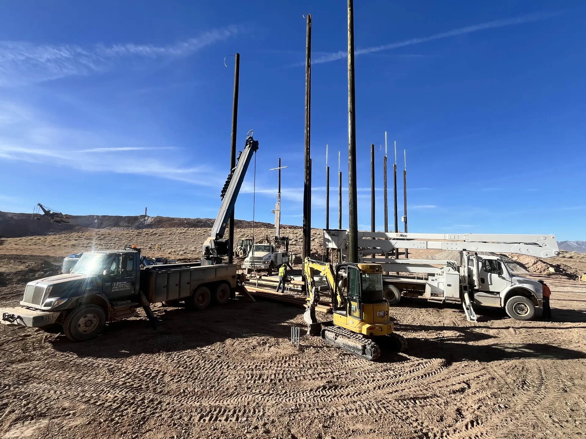Pole Line Contractors trucks and equipment alongside utility poles at a field project.